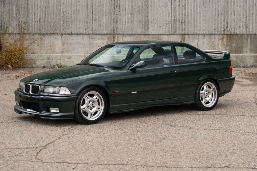 Green BMW car parked on a concrete surface with a gray wall in the background
