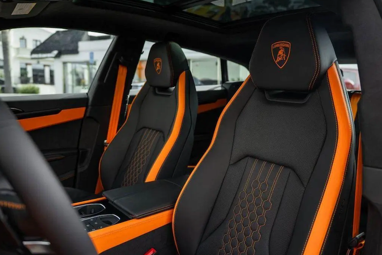 Luxury car interior with black and orange seats featuring a logo.