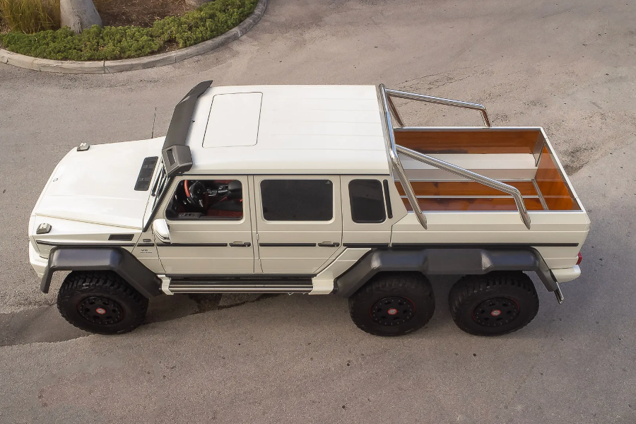 White off-road vehicle with a wooden bed on a paved surface