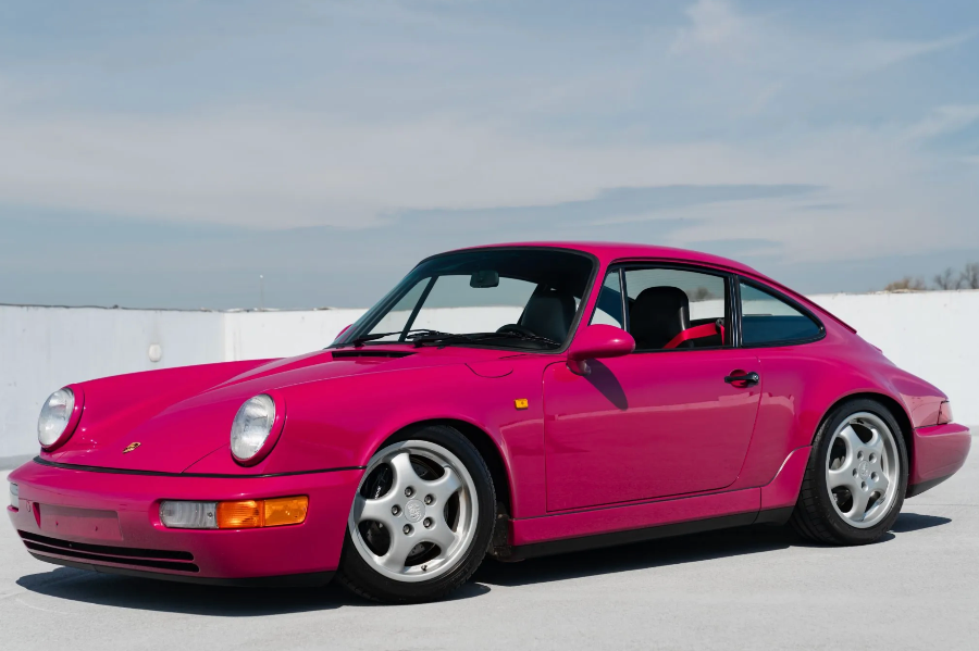 Pink Porsche car on a clear day with a white wall in the background