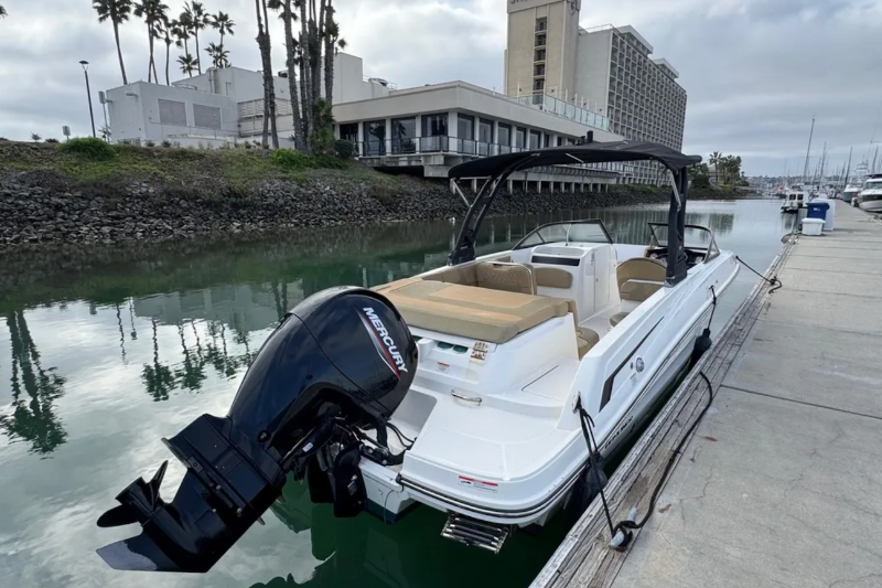 White pontoon boat with black outboard motor docked at a marina.