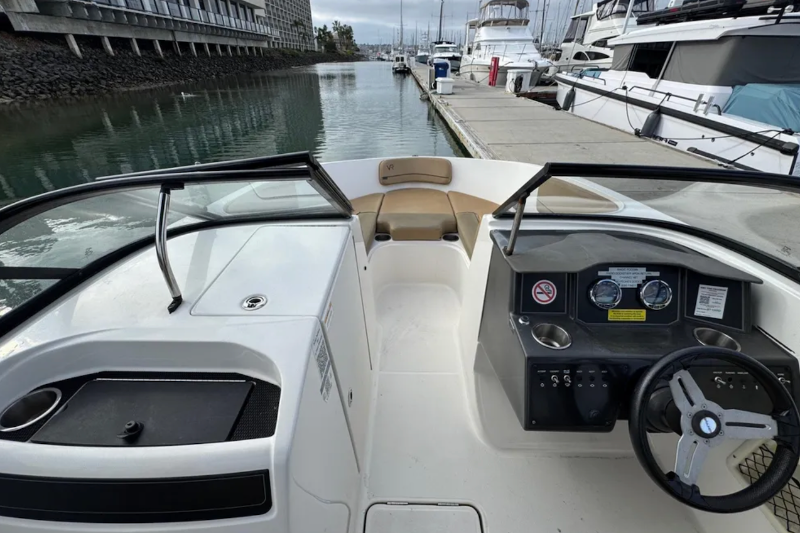 Boat interior with dashboard and steering wheel, docked at a marina.