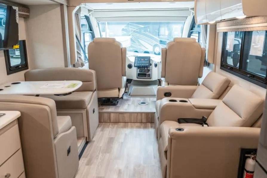 Interior of a modern RV with beige seating and electronic displays.