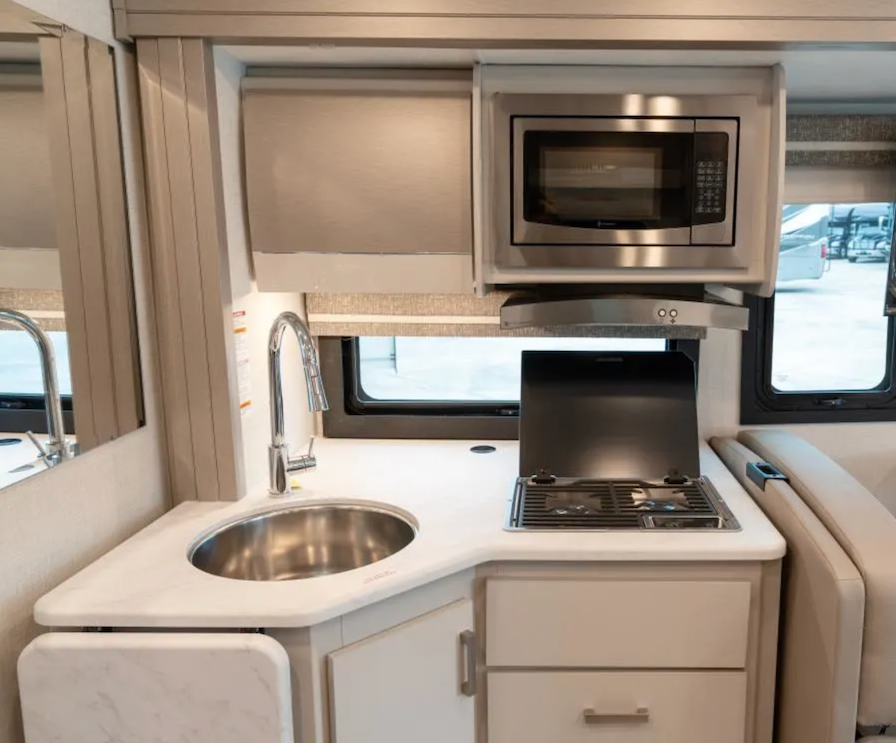 Compact kitchen setup inside a vehicle with microwave, stove, and sink.