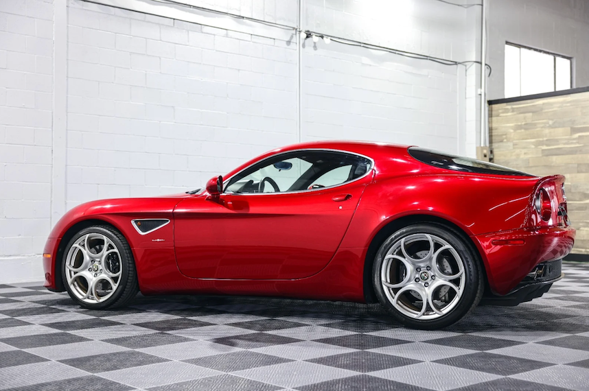 Red sports car in a showroom with white walls and checkered floor.