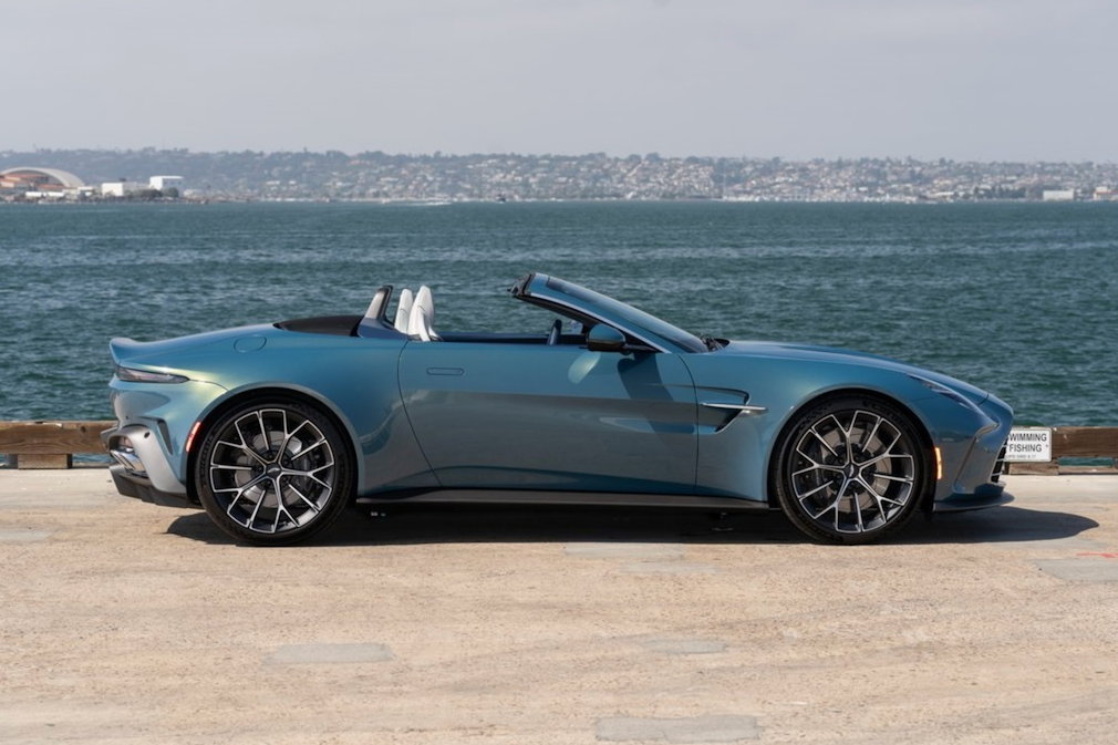 Blue convertible car parked on a wooden platform with water and skyline in the background