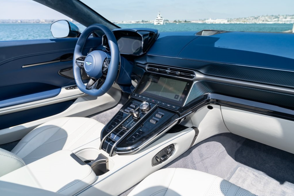 Car interior with steering wheel and dashboard, featuring a waterfront view through the windshield.