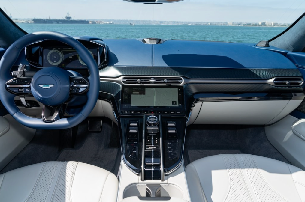 Car interior with steering wheel and dashboard view, featuring a waterfront background.