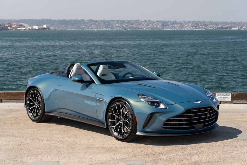 Blue convertible car parked by a waterfront with a clear sky.
