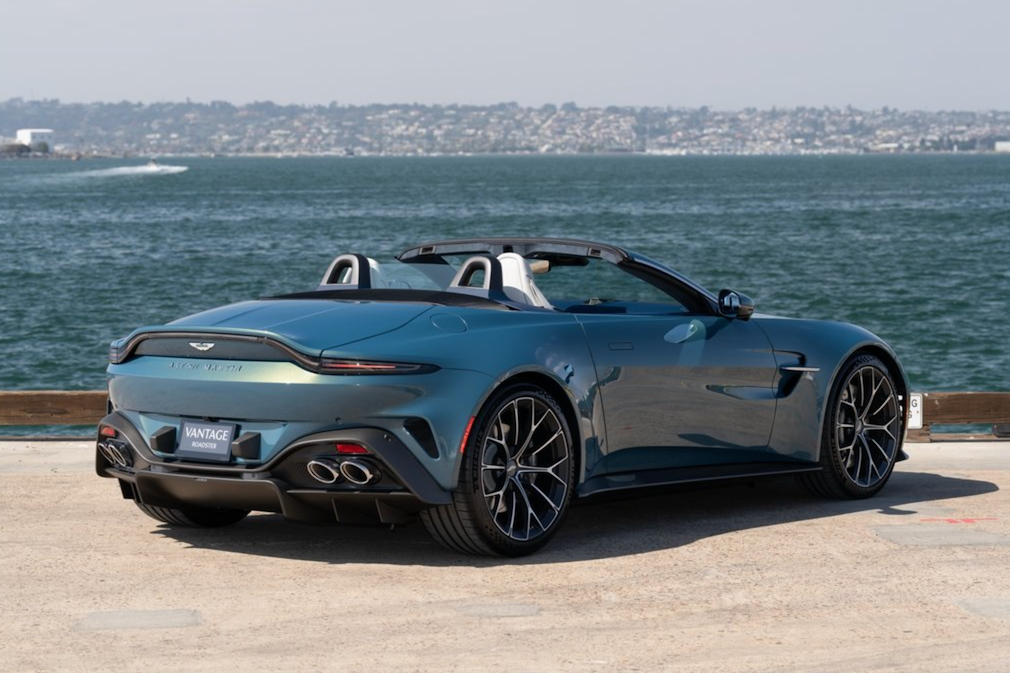 Gray convertible sports car parked by a waterfront with a cityscape in the background