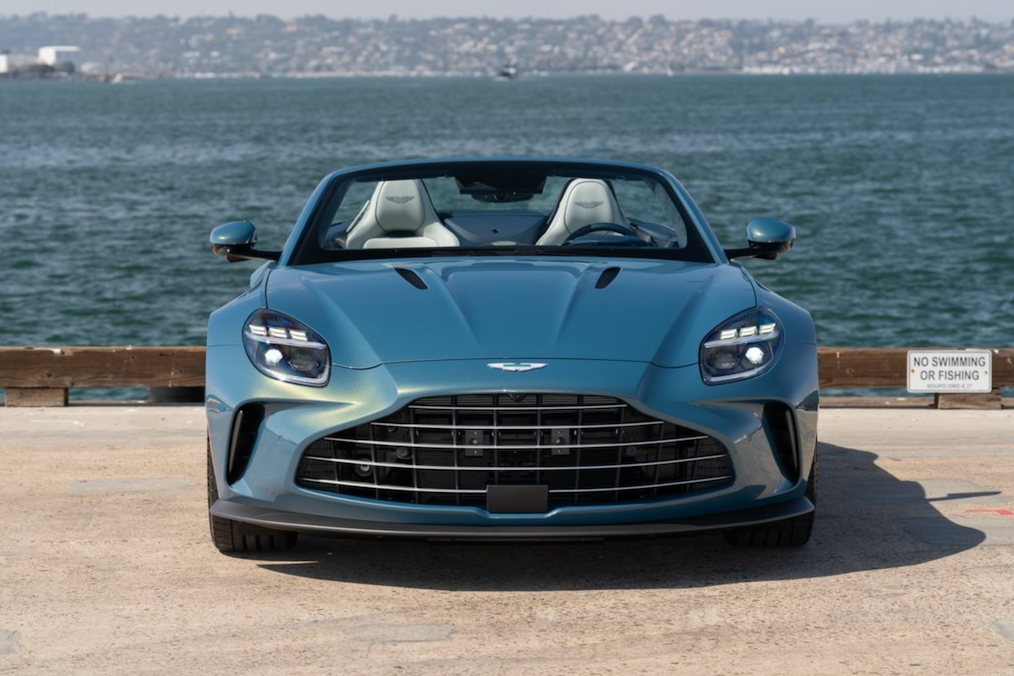 Blue convertible car parked by a waterfront with water and sky in the background