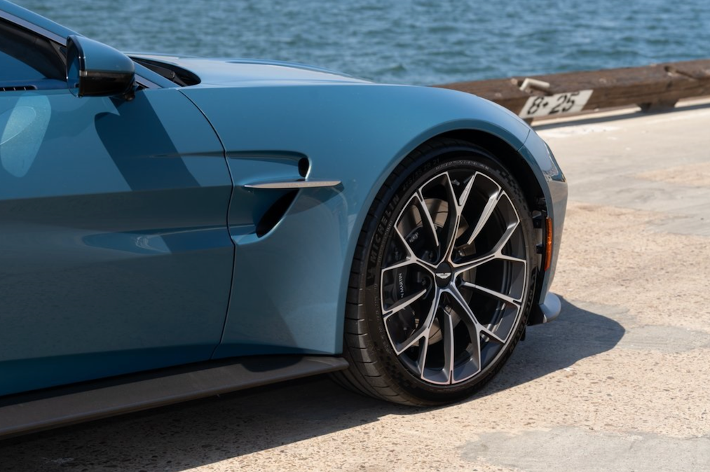 Close-up of a blue car's wheel and side profile by a waterfront.