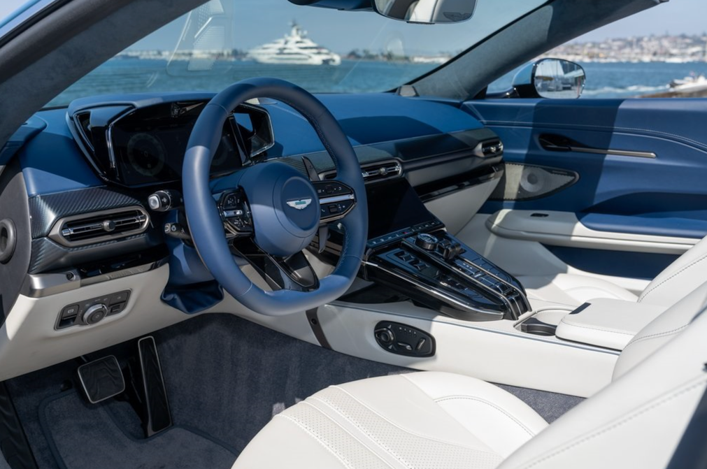 Car interior with steering wheel and dashboard, featuring a waterfront view through the windshield.