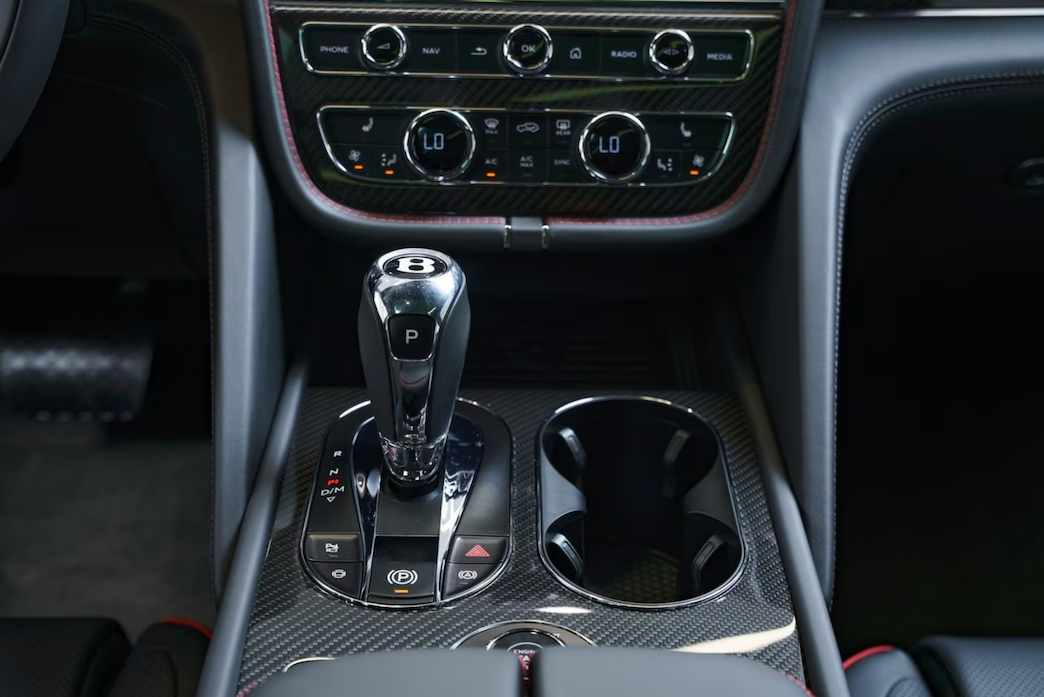 Car interior with gear shift and cup holder featuring Bentley logo.