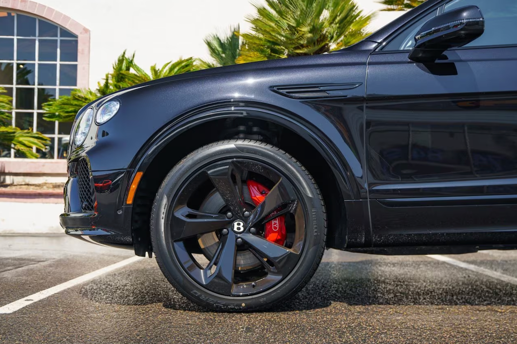 Close-up of a black car's wheel with red brake calipers on a street.