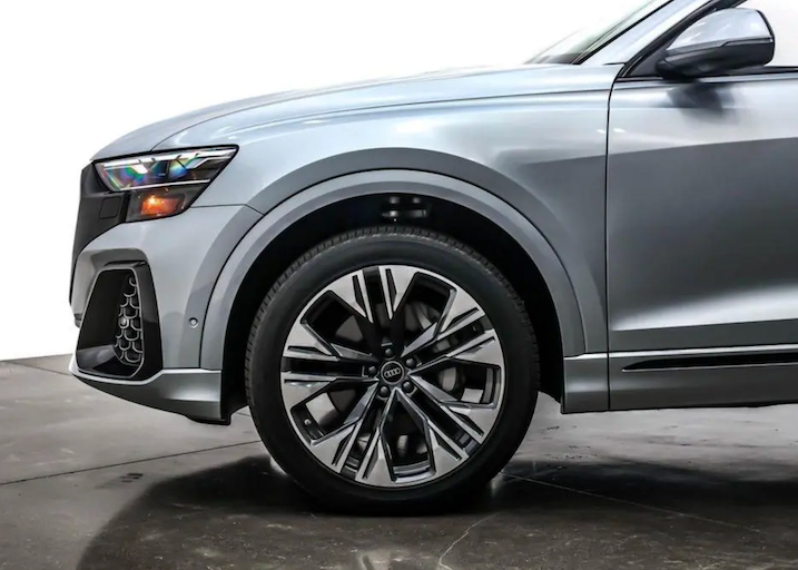 Close-up of a silver Audi SUV wheel and part of the car body on a gray background