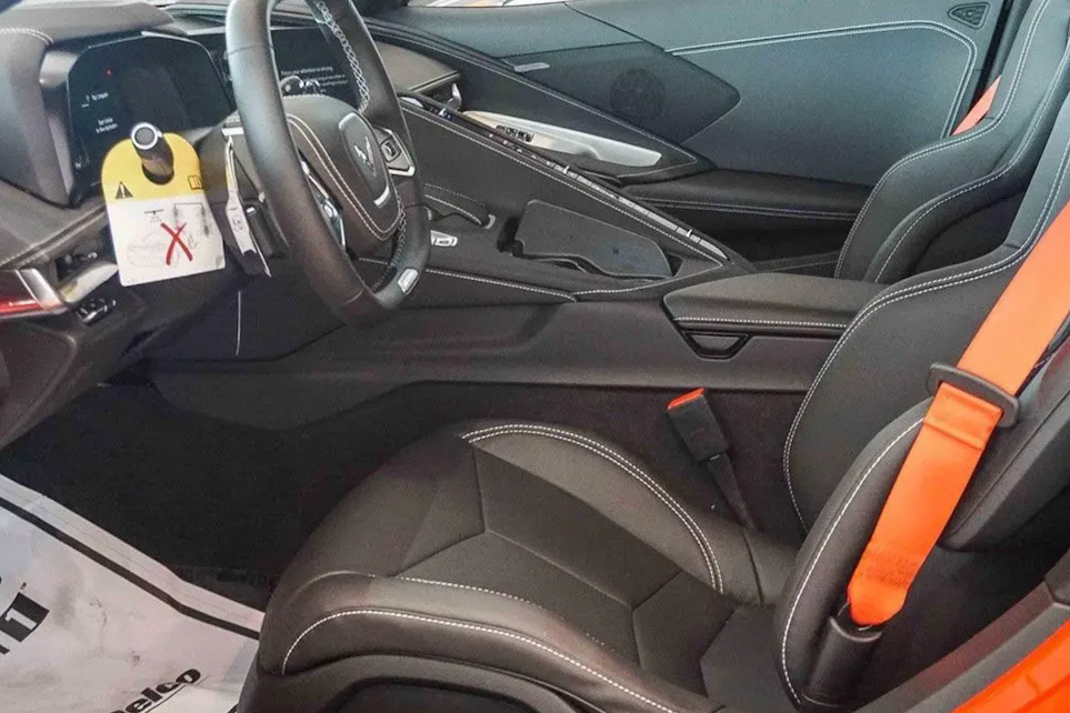 Car interior with orange seat belts and a visible brand logo on the steering wheel.