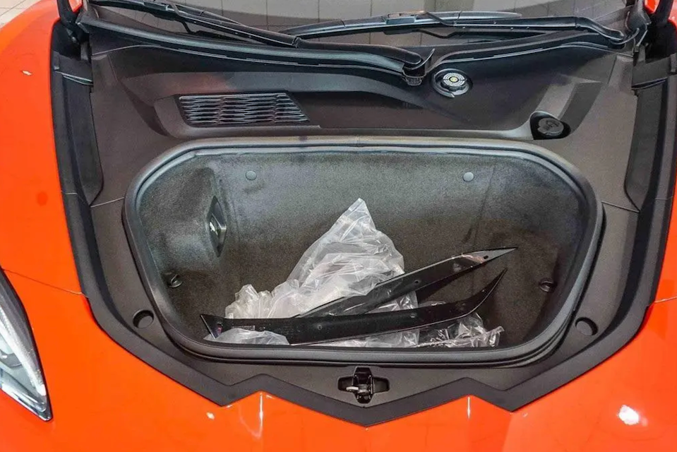 Open car hood with a plastic bag inside, on an orange car.