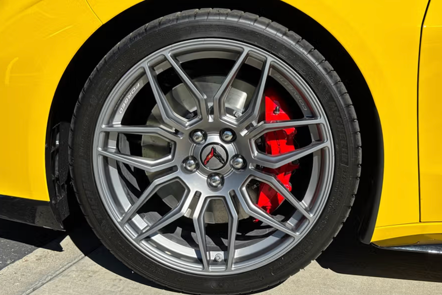 Close-up of a car wheel with a yellow vehicle, silver rim, and red brake caliper.