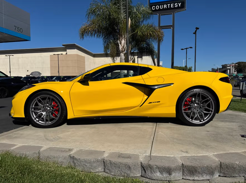 Yellow sports car parked in front of a dealership with palm trees in the background.