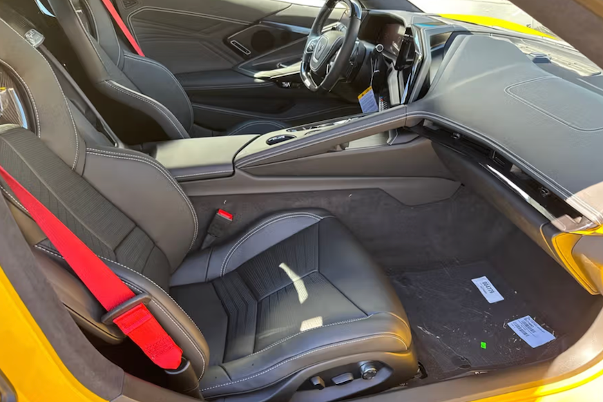 Car interior with black seats and red accents, showing dashboard and steering wheel.