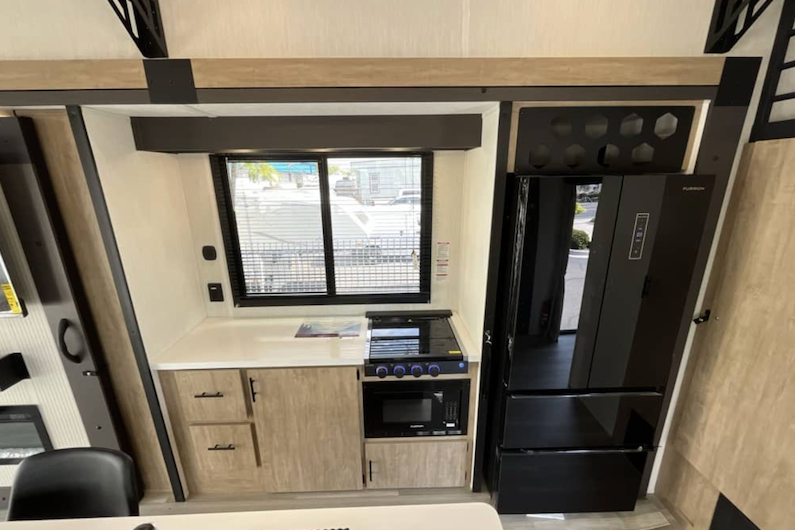 Compact kitchen area inside a vehicle with refrigerator, stove, and cabinets.