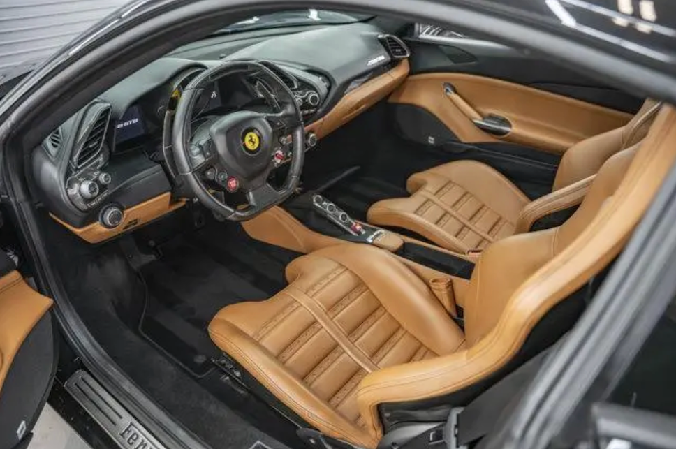 Luxury car interior with tan leather seats and steering wheel, featuring a Ferrari logo.