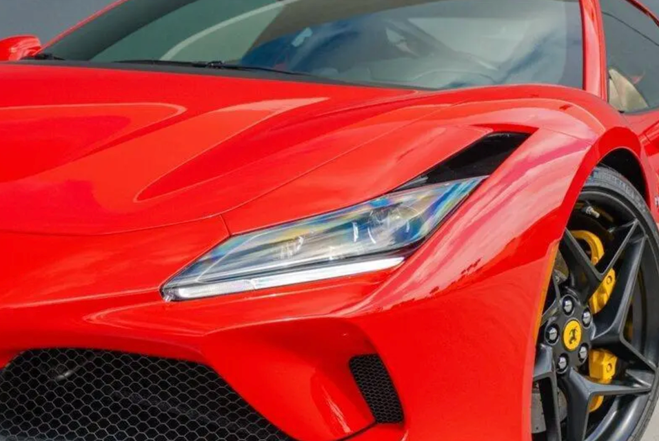 Close-up of a red sports car's front headlight and grille.