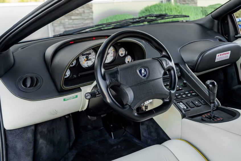 Car interior with steering wheel and dashboard, featuring a Lamborghini logo.