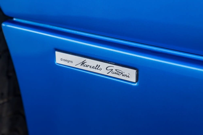 Blue vehicle with a 'Marcello Gandini' badge on a blurred background