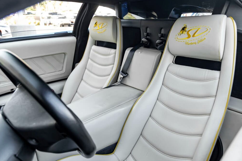 Car interior with white leather seats and a steering wheel, featuring a logo on the headrest.
