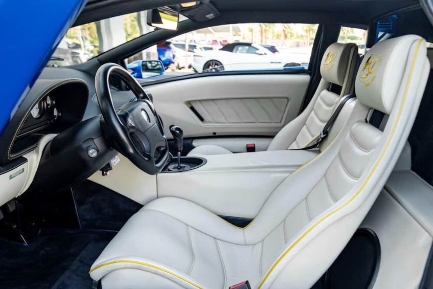 Car interior with white seats and yellow stitching, showing dashboard and steering wheel.