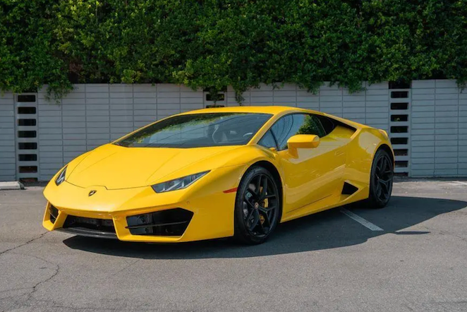Yellow sports car parked on a concrete surface with greenery in the background