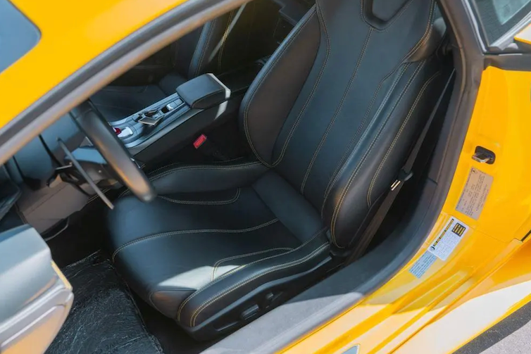 Close-up of a car's black interior seat and dashboard with yellow exterior.