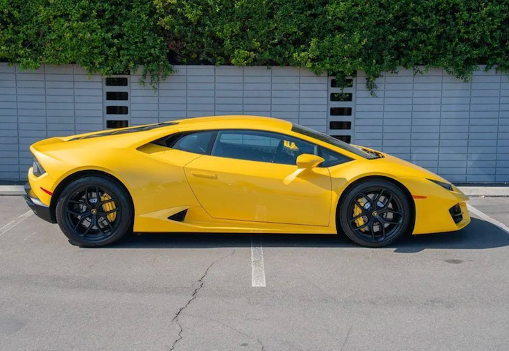 Yellow sports car parked in a parking lot with a building and greenery in the background