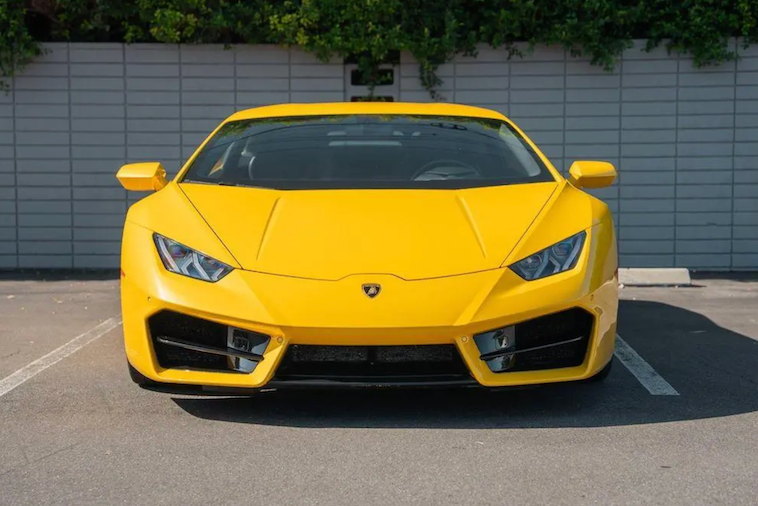 Yellow Lamborghini sports car parked in a lot with a gray wall and greenery in the background