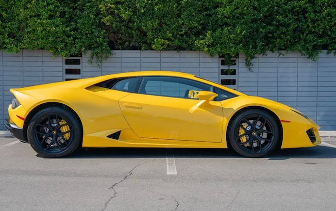 Yellow sports car parked on a street with greenery in the background