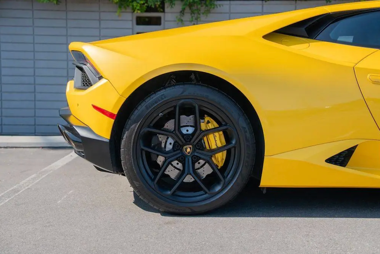Yellow sports car with black rims parked on a concrete surface.