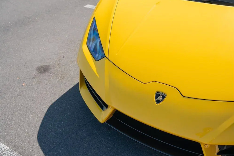Close-up of a yellow sports car with a visible logo on a road.
