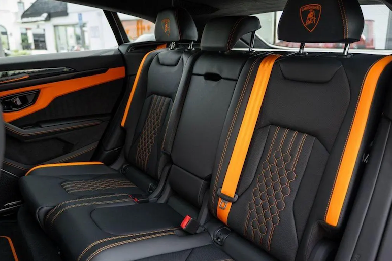 Car interior with black and orange seats featuring a logo on the headrest.