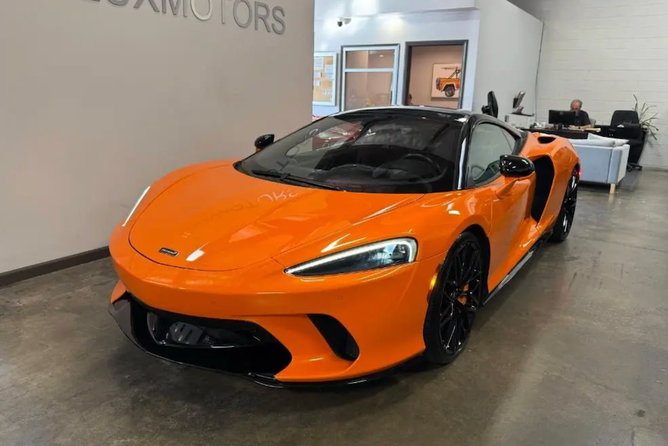 Orange sports car in a showroom with 'Aston Martin' branding.