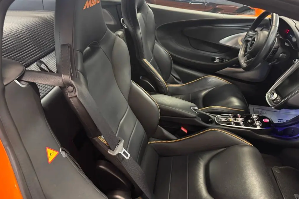 Car interior with black leather seats and steering wheel, featuring the McLaren logo.
