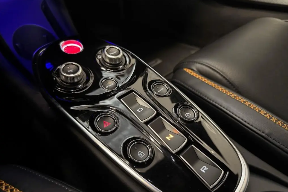 Close-up of a car's gear shift lever with control buttons on a black interior background.