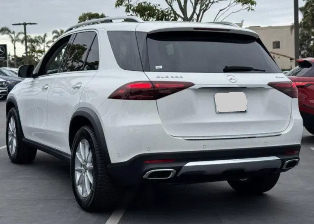White Mercedes-Benz SUV parked on a paved surface with a building and trees in the background.