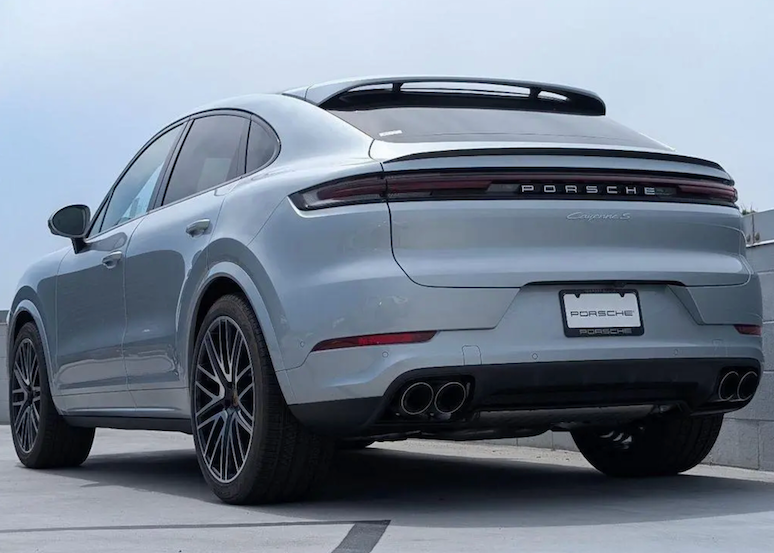 Gray Porsche SUV parked on a concrete surface with a light blue sky background