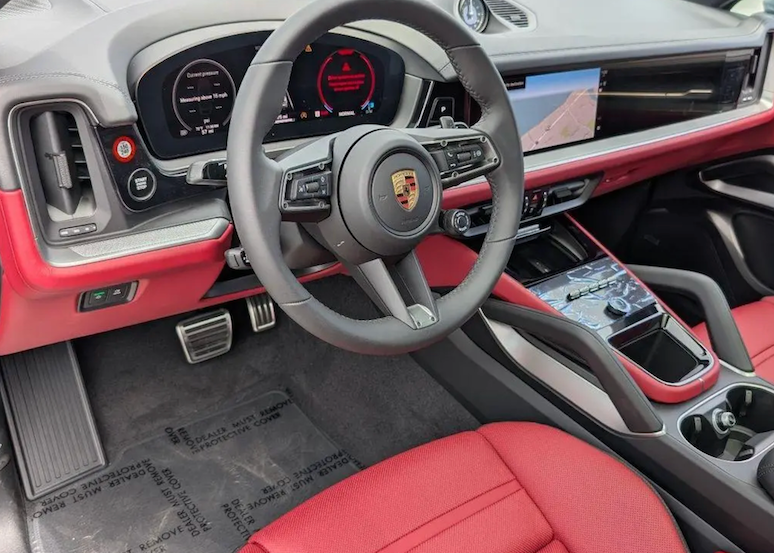 Car interior with red and gray design, featuring a Porsche logo on the steering wheel.