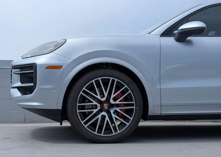 Close-up of a car wheel with a visible Porsche logo on a gray background
