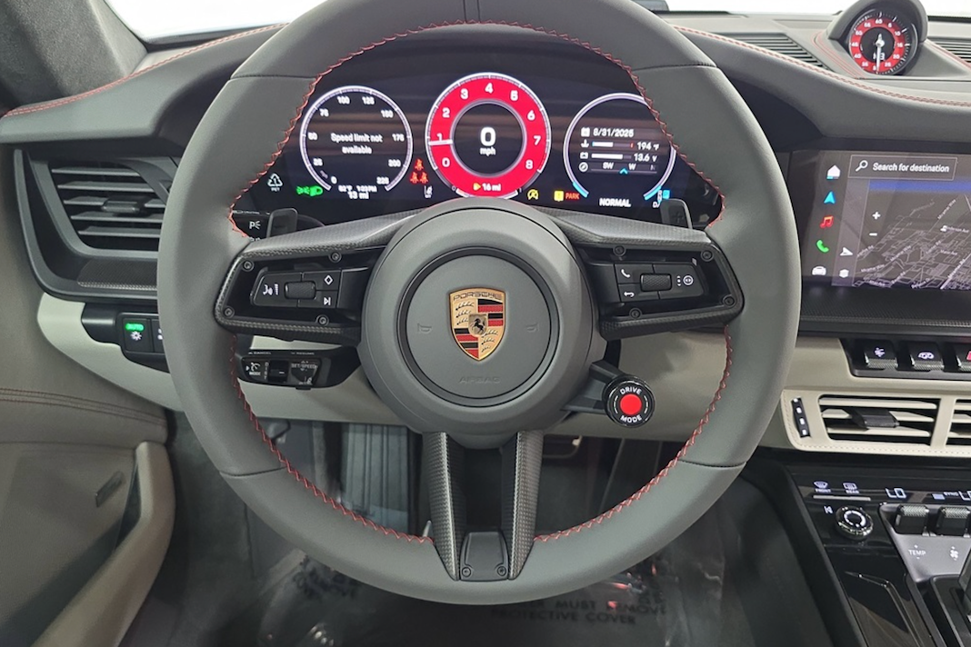 Steering wheel of a Porsche car with digital dashboard display.