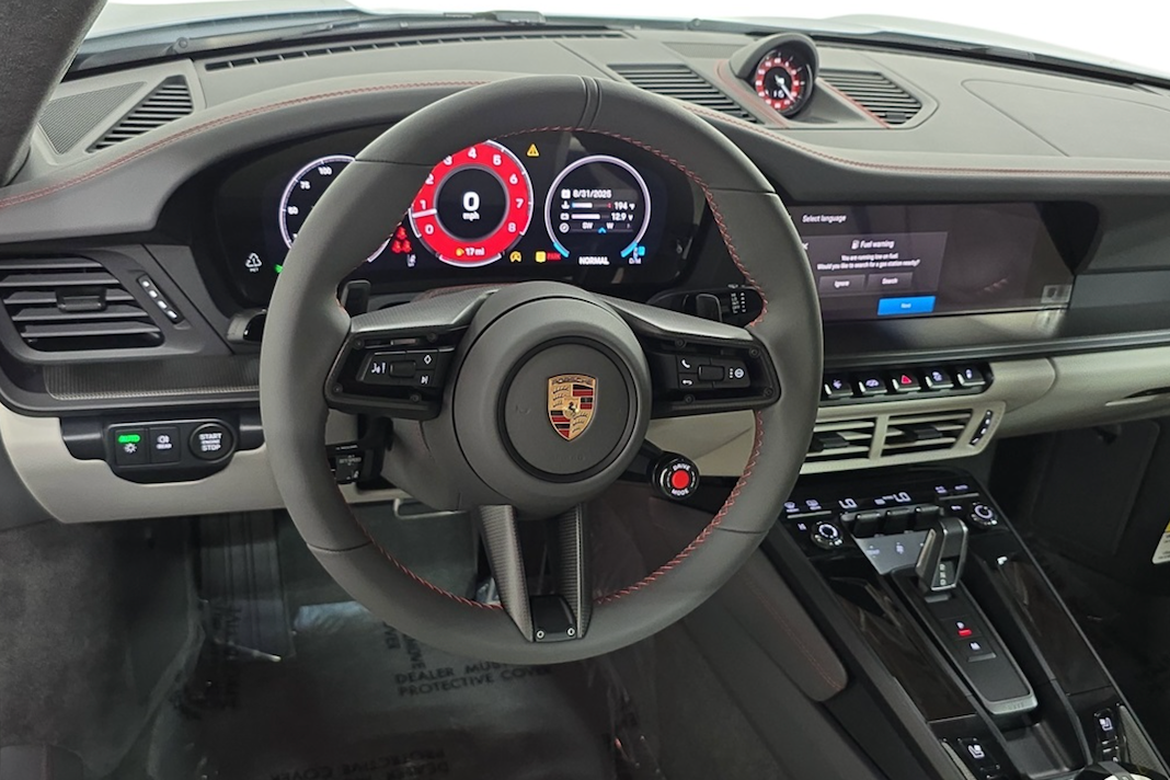 Car interior with steering wheel and dashboard display, featuring a Porsche logo.