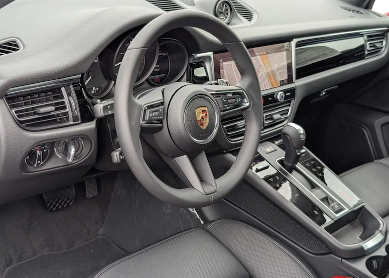 Car interior with steering wheel and dashboard featuring a Porsche logo.